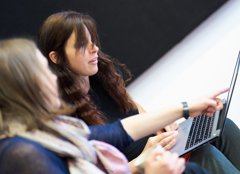 Two team members sitting next to each other pointing at a laptop and talking to each other