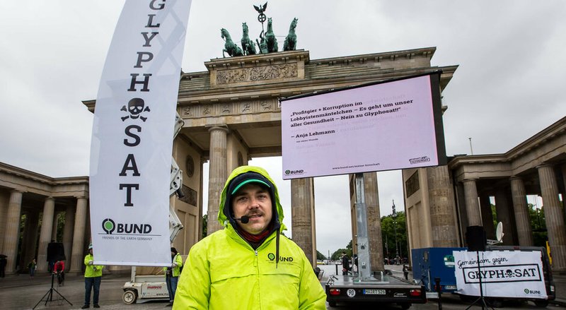 Aktion vor dem Brandenburger Tor mit großer Leinwand und einem Aktivisten in gelb-grüner Jacke